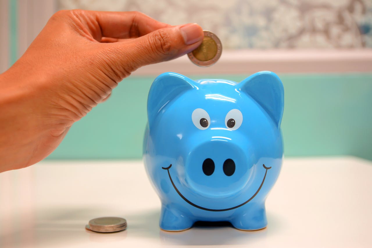 person putting money into a blue piggy bank