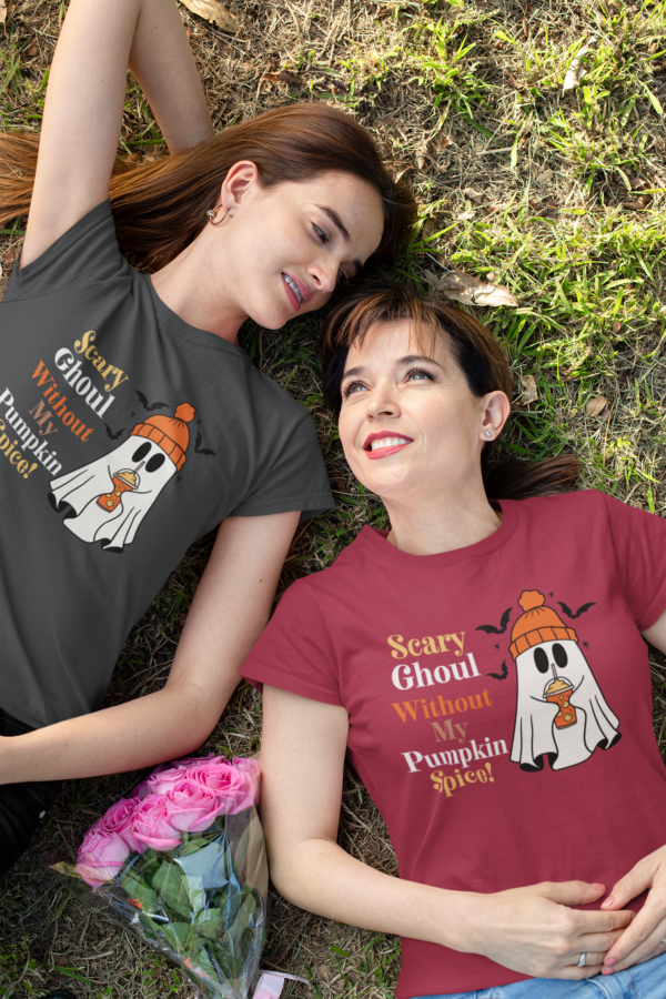 Two women laying in the grass wearing t-shirts that have a ghost holding a latte that says Scary Ghoul Without My Pumpkin Spice.