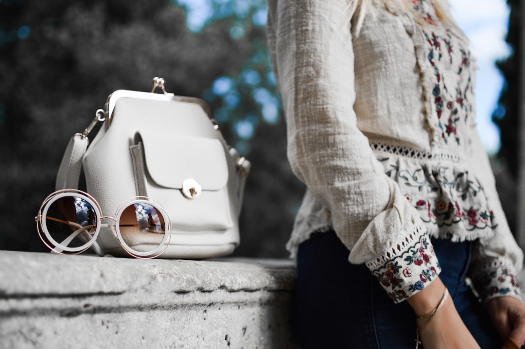 Photo by Tamara Bellis woman wearing beige and red floral top leaning on gray concrete slab with white leather bag ontop